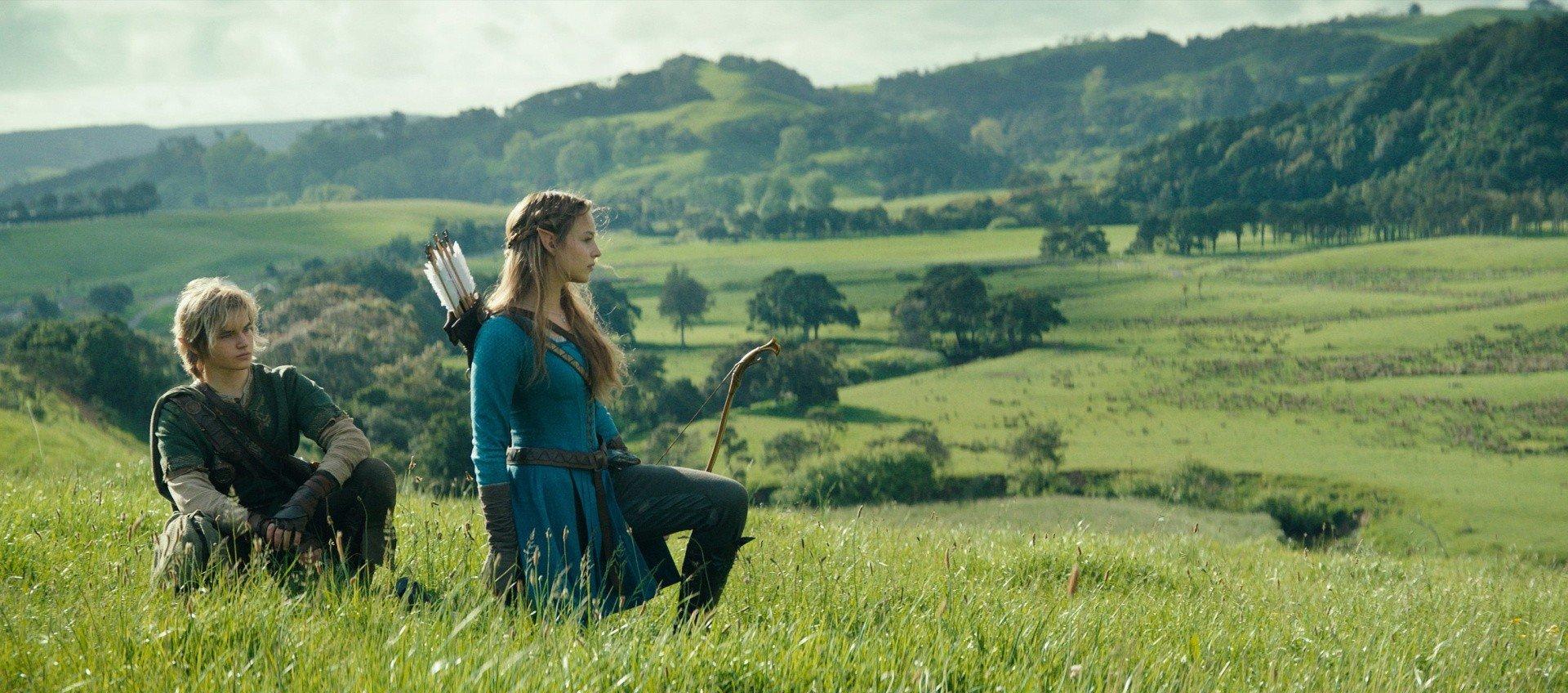 Two characters on a hill overlooking fields with sporadic trees. They have elf like ears. A female character has long brownish hair and a bow and arrow. The male character has shorter, lighter coloured hair.

They are Link and Zelda from the new live action movie adaptation.