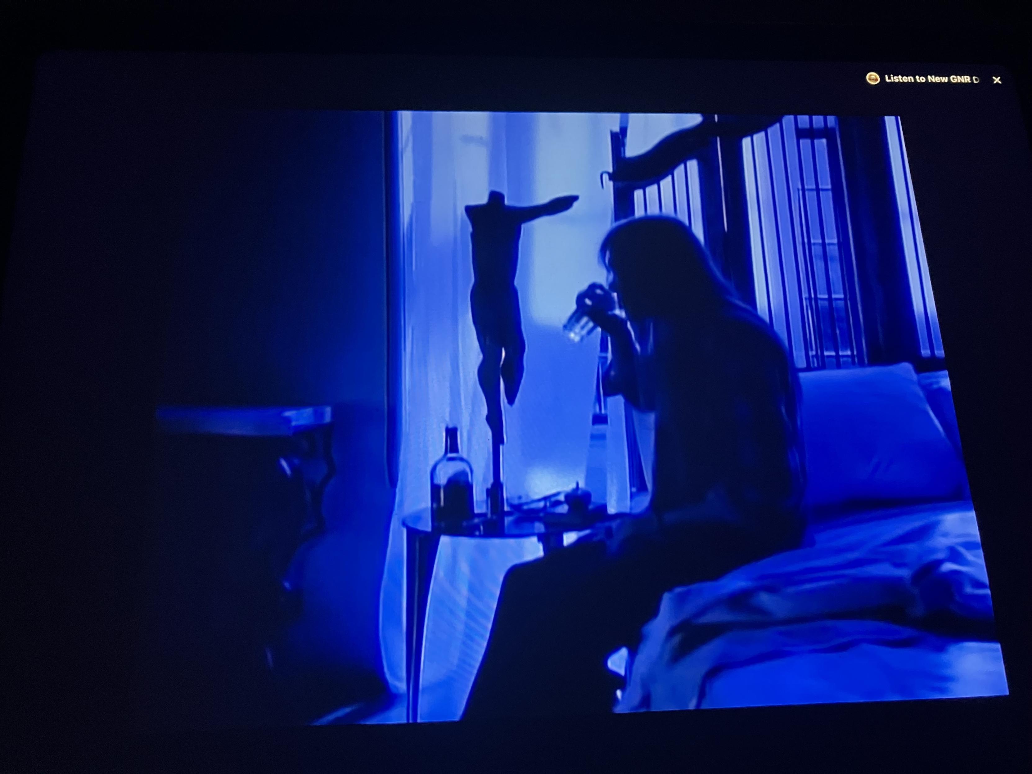 A gloomy image of a man sitting on their bed, drinking from a glass.