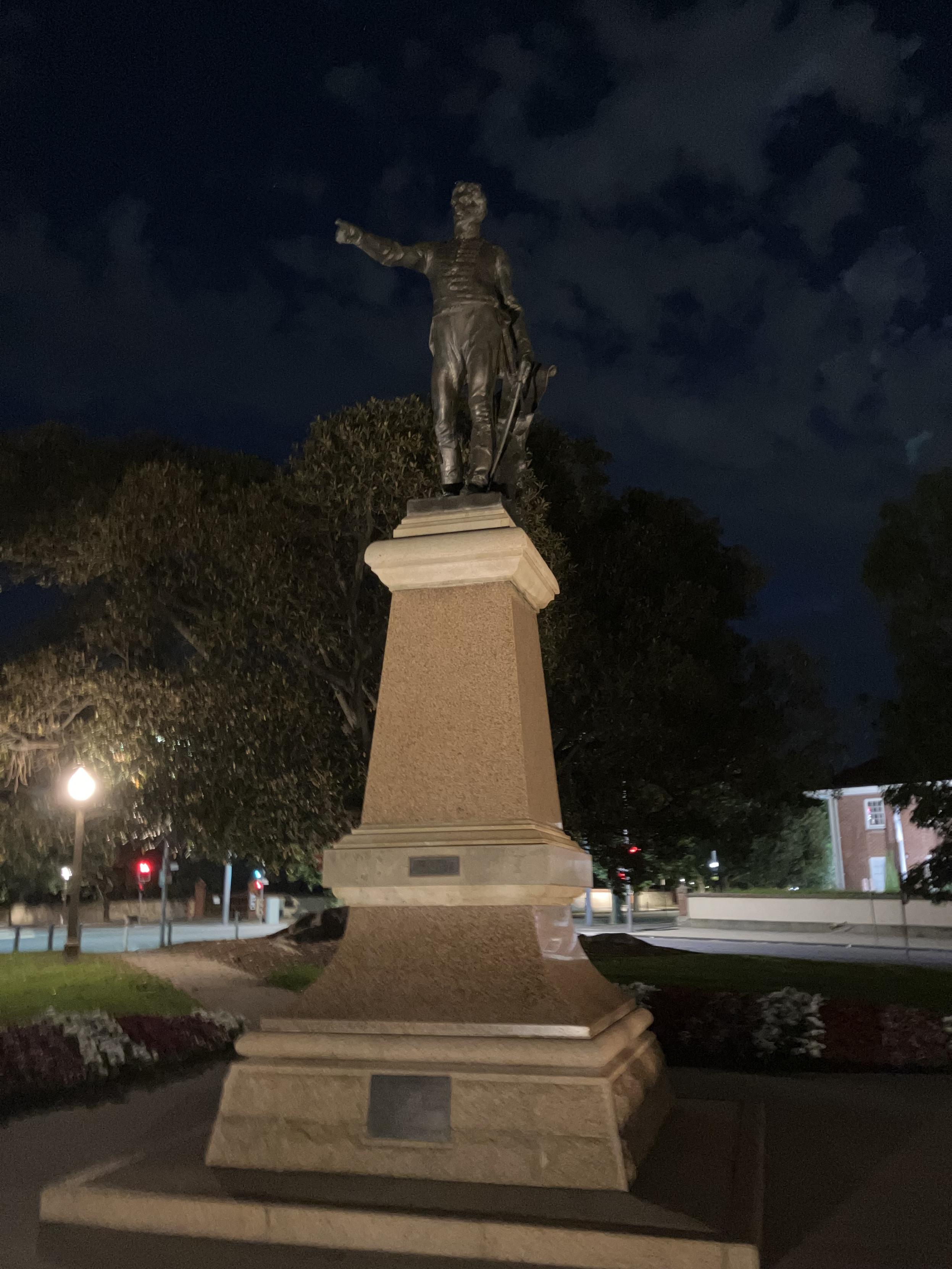 A statue of a british colonial looking dude, pointing forward and off to the left of frame. 

It is still pre-dawn, with some light enering the sky.