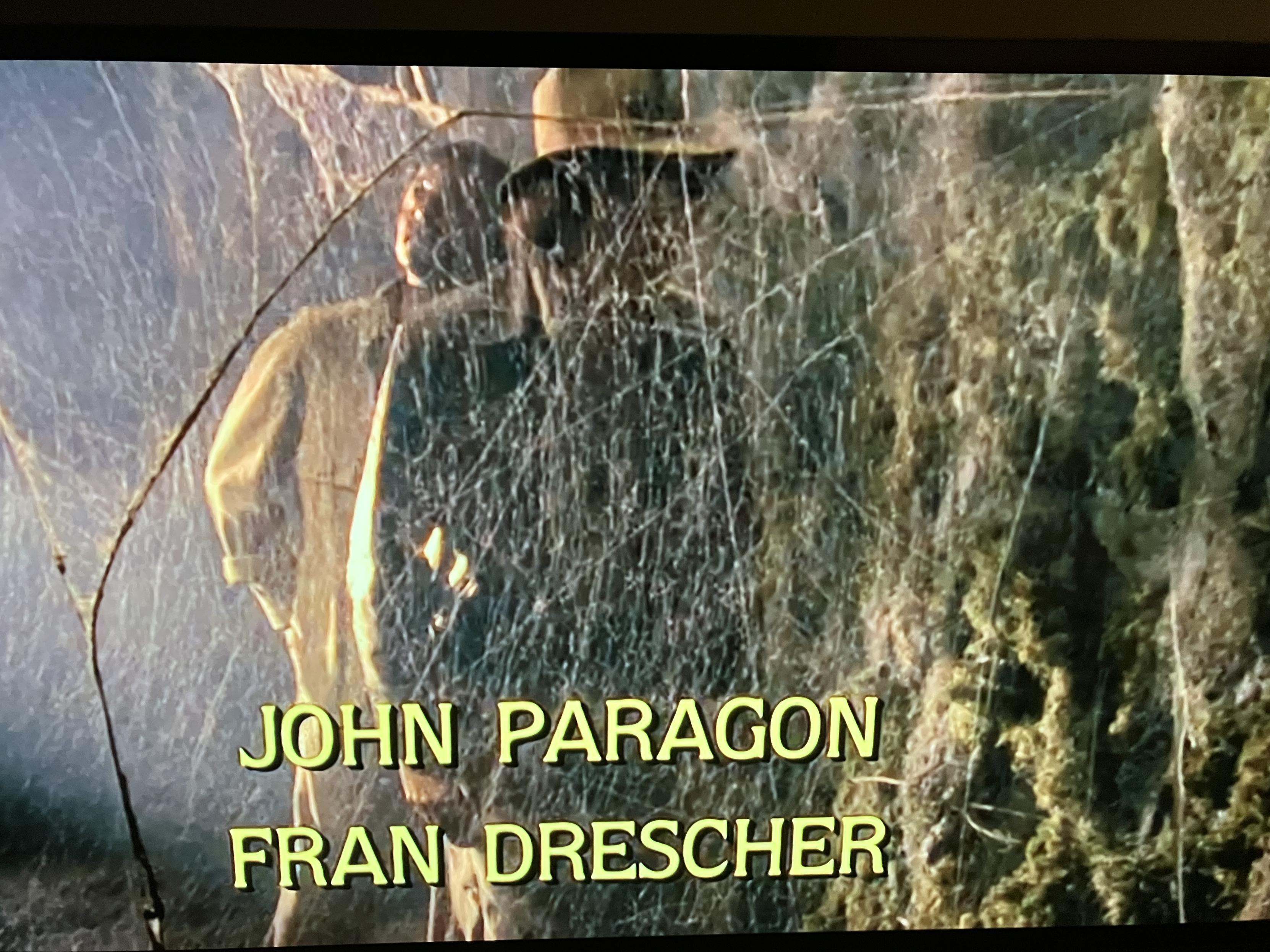 Image from a film of two tomb explorers approaching a spiderweb. 

Overlaid is cast listings:
John Paragon
Fran Drescher